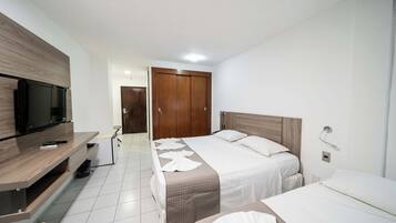 Una habitación de hotel con dos camas, televisión, armario de madera y suelo de baldosas blancas.
