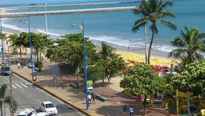 Una calle frente a la playa con palmeras, un camino para peatones y vista al océano.