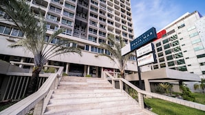 Entrada de hotel con una escalera moderna, palmeras y un letrero que dice 'Hotel Praia Mar'.