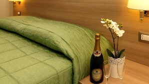 A neatly made bed with a green blanket, a bottle of champagne, two glasses, and a decorative orchid plant on a bedside table. - Hotel Argentina (Rome)