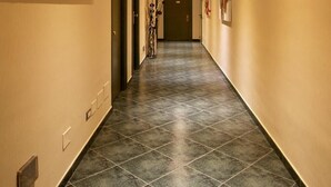 A hotel hallway with a long, tiled floor, beige walls, and a painting of red flowers on the left wall. - Hotel Argentina (Rome)