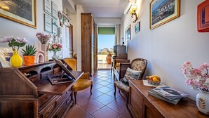 A hallway with a wooden desk, chairs, framed pictures, and a view to the outside. - Alla Dimora Altea (Florence)