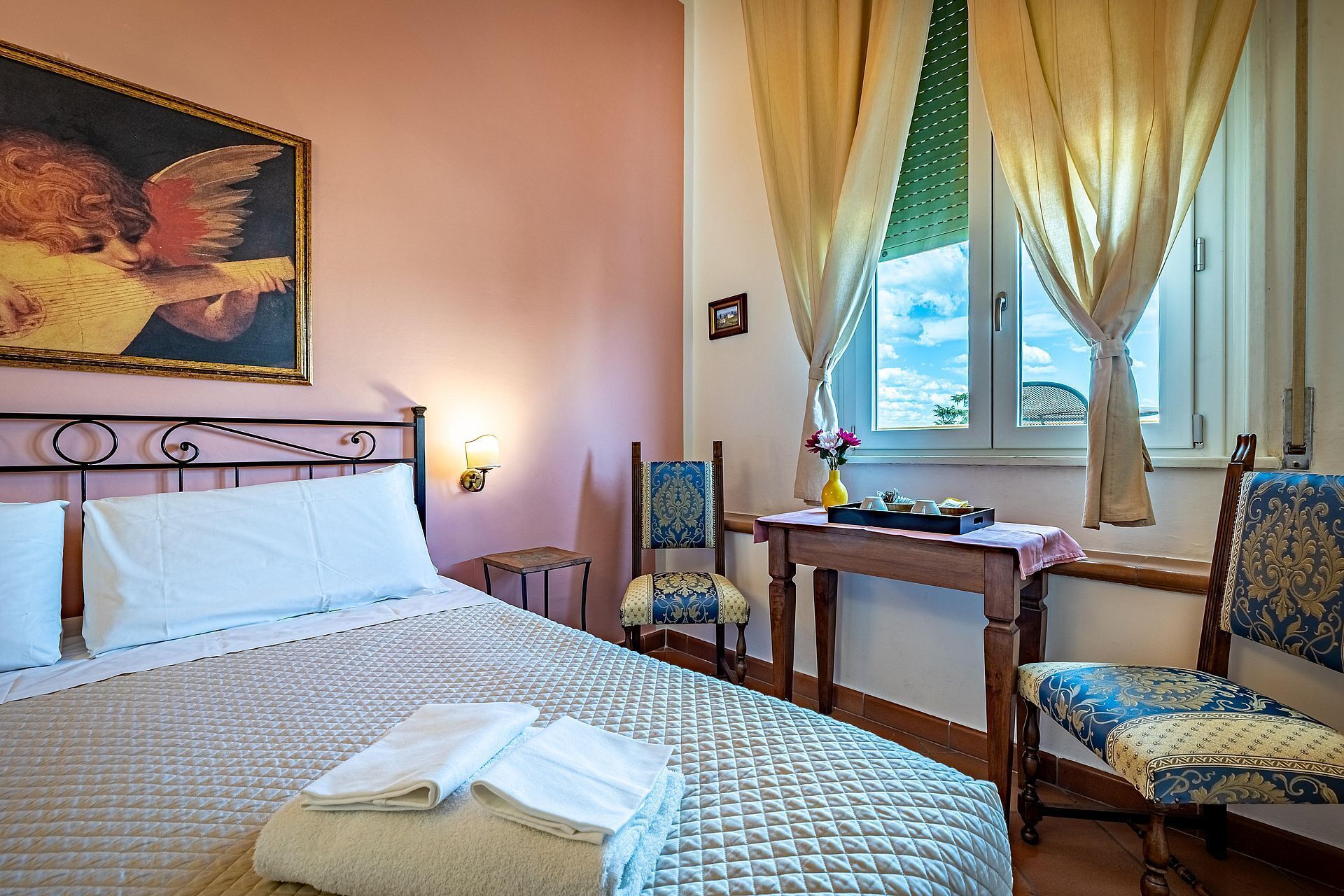 A hotel room with a bed, a chair, a small table, and a window with curtains.