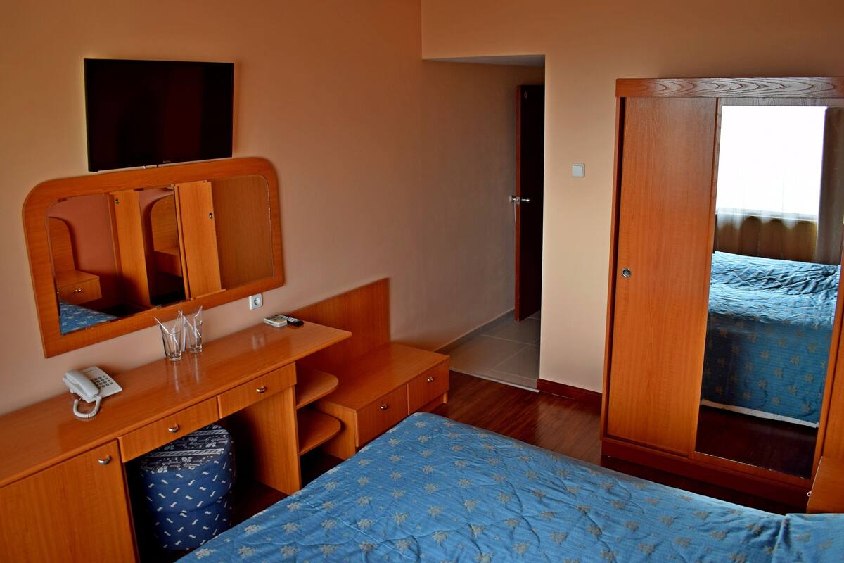 Una habitación de hotel con una cama, un escritorio de madera con teléfono, un espejo y un armario.