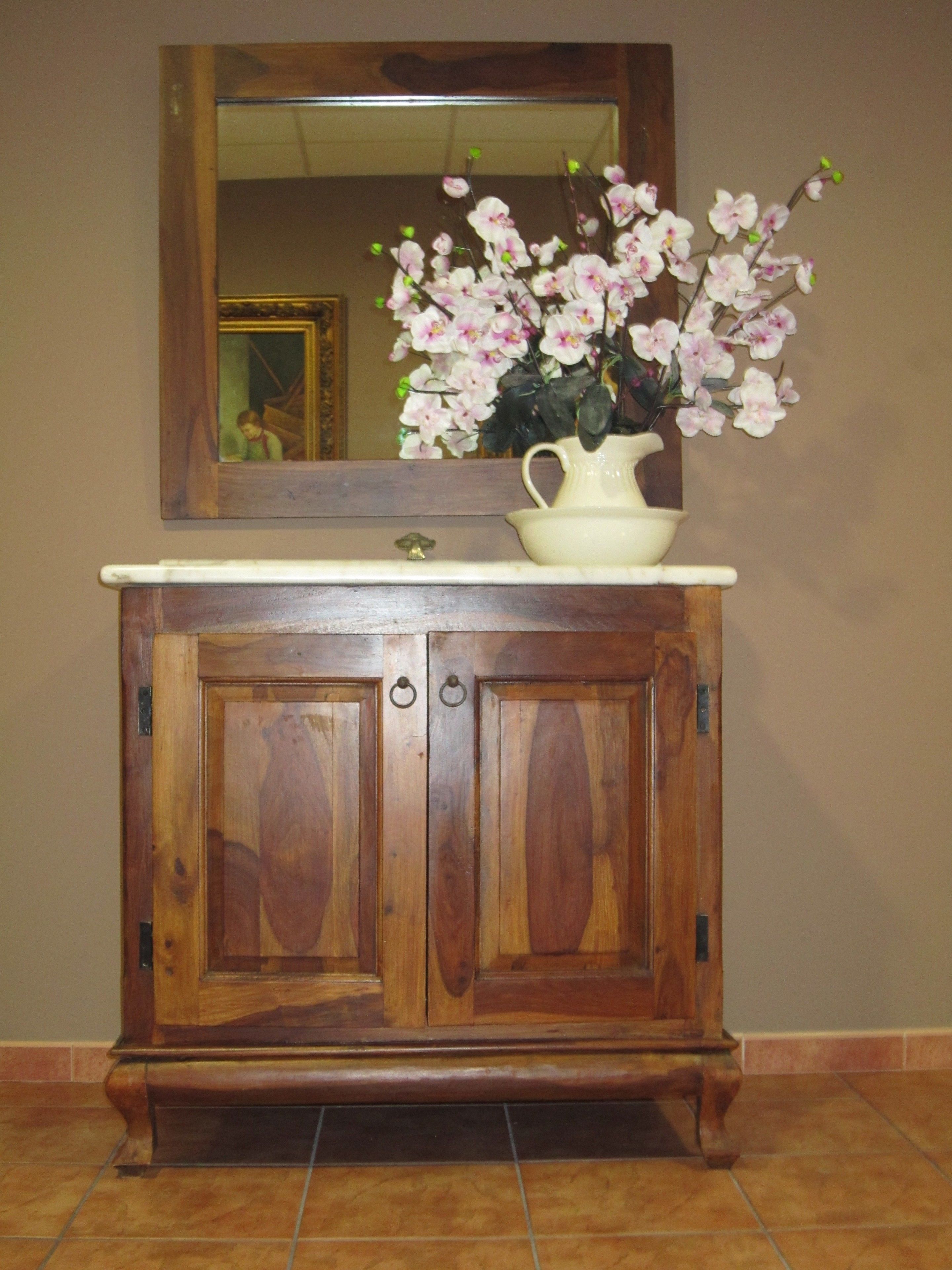 Un mueble de madera con un espejo encima, un jarrón con flores y un suelo de baldosas.