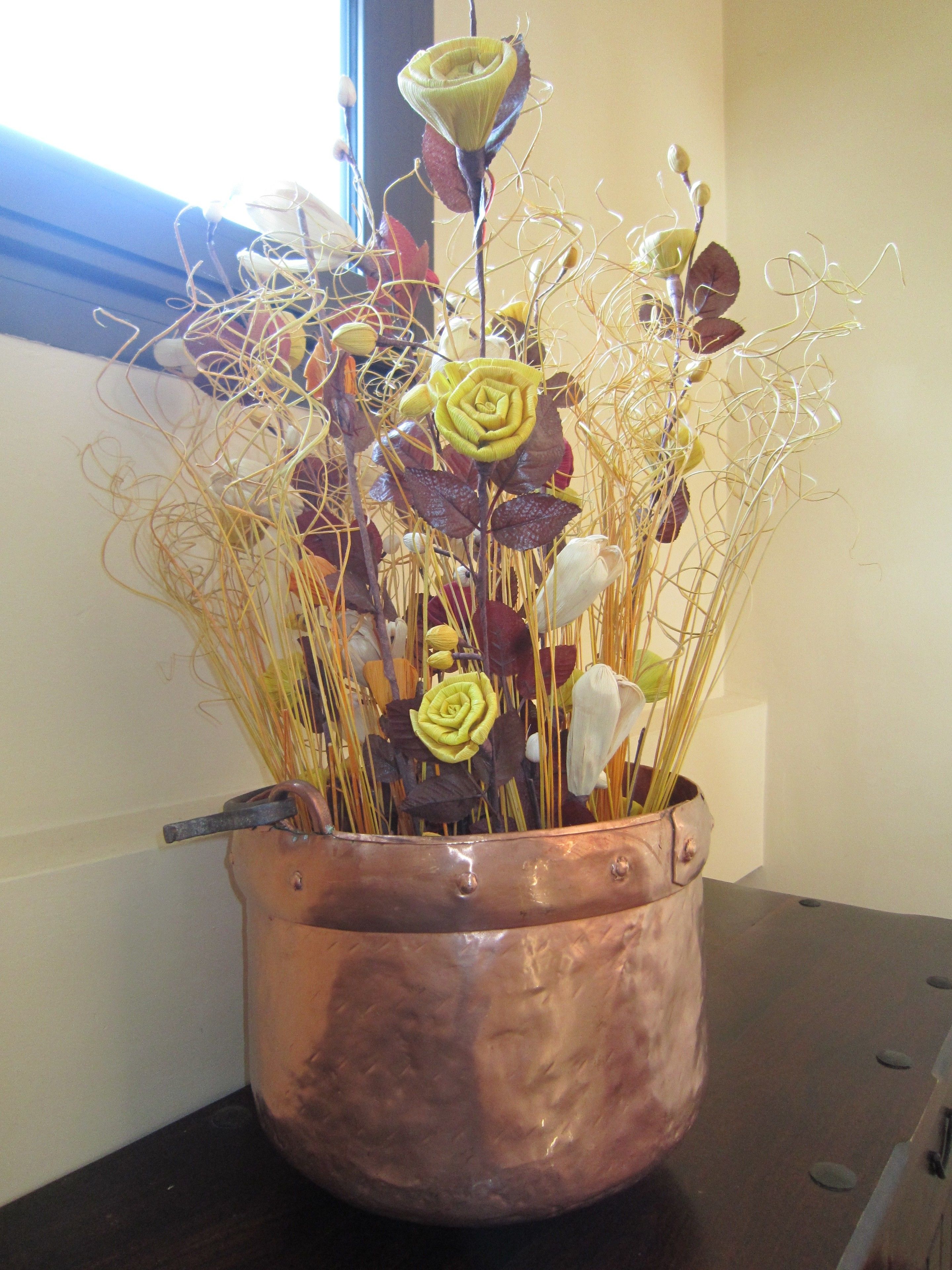 Un jarrón de cobre con un arreglo floral sobre una mesa de madera.
