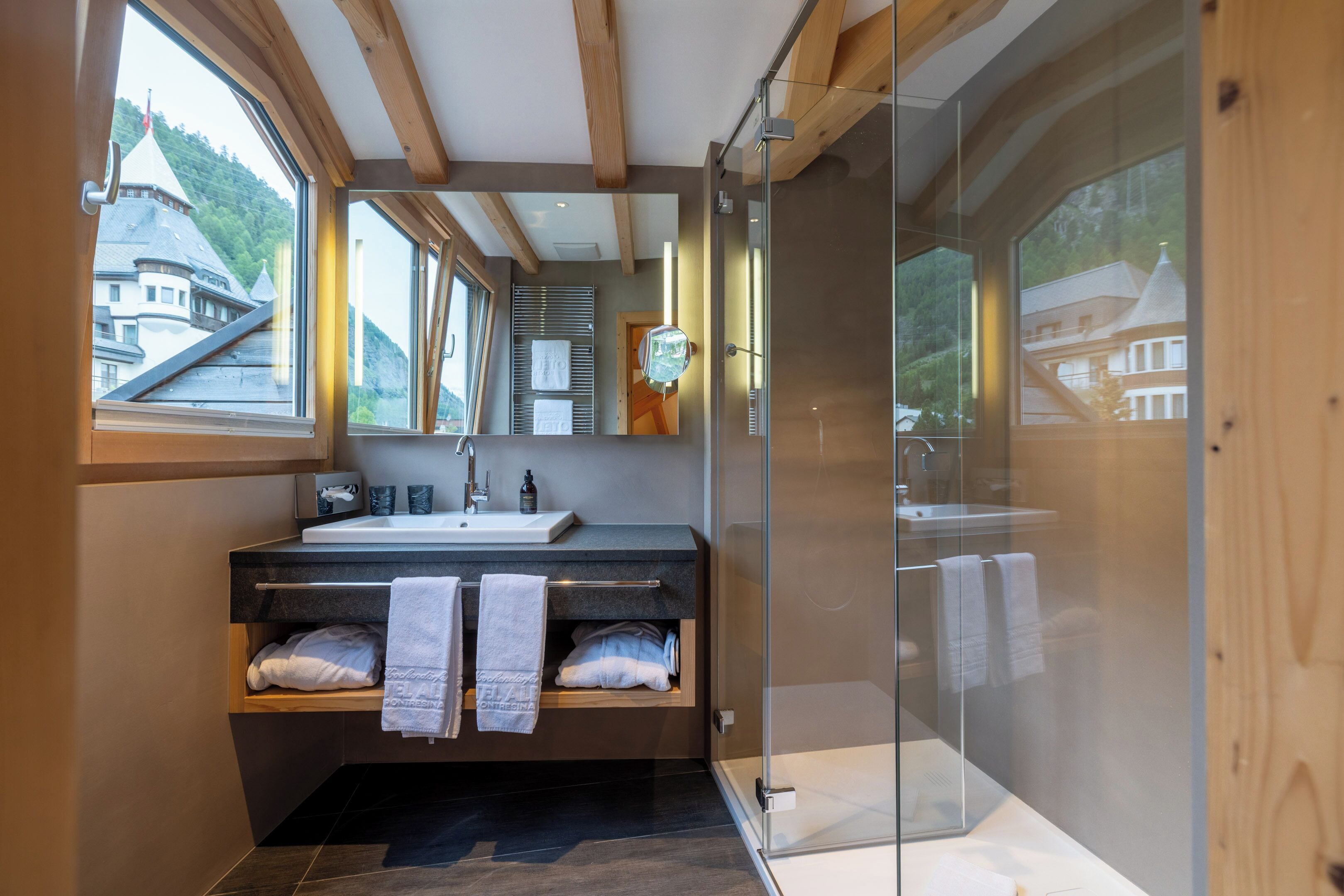 Un bagno moderno con cabina doccia in vetro, soffitto in legno e un'ampia finestra che si affaccia su un edificio.