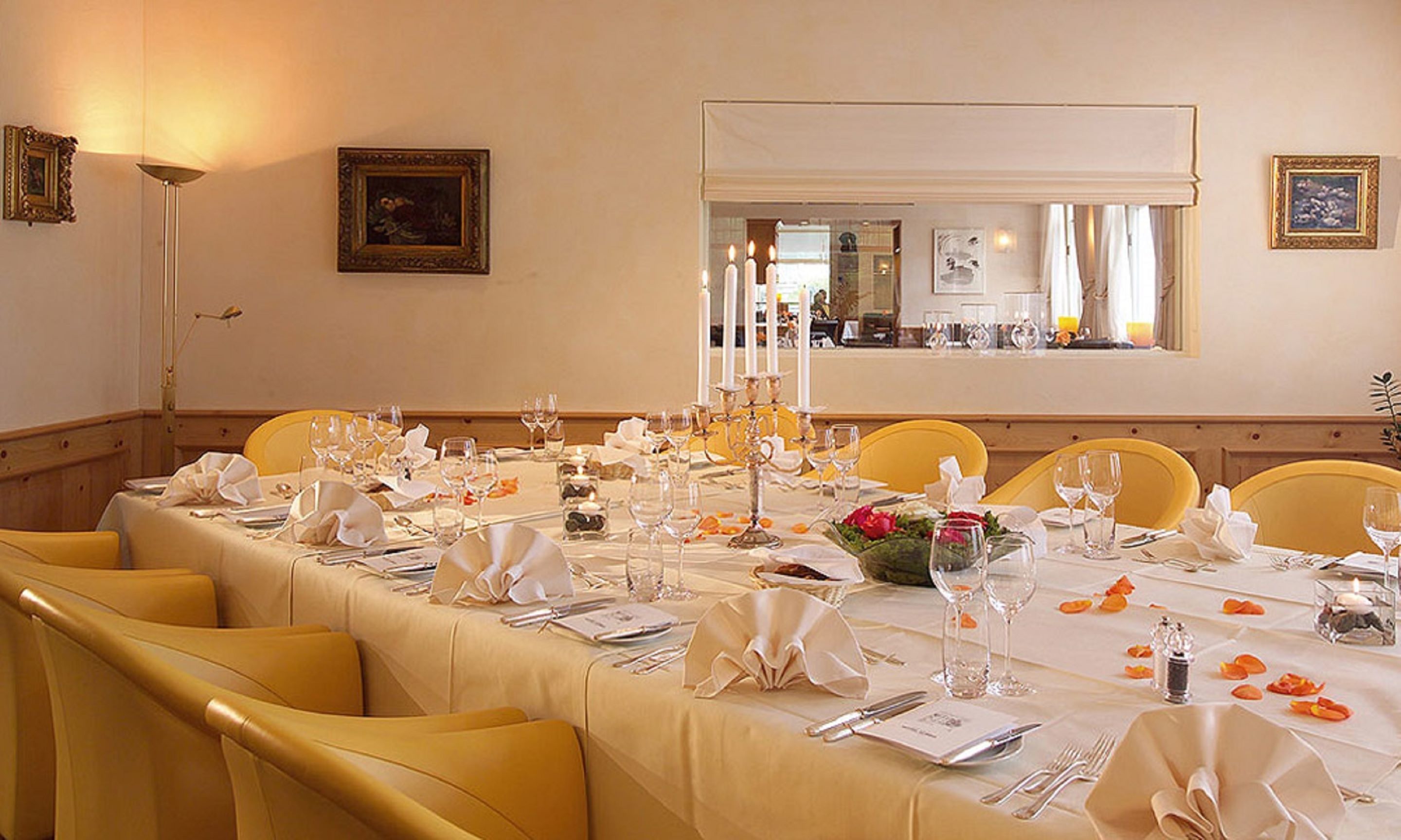 Un coin repas avec une longue table dressée pour le repas, des chaises jaunes et un miroir qui reflète la pièce.
