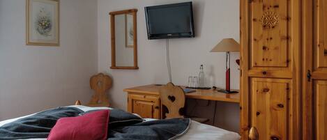 Un dormitorio con cama, un escritorio de madera, televisor y armario.