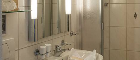Un baño moderno con cabina de ducha de vidrio, un lavamanos blanco con espejo y un perchero para toallas.