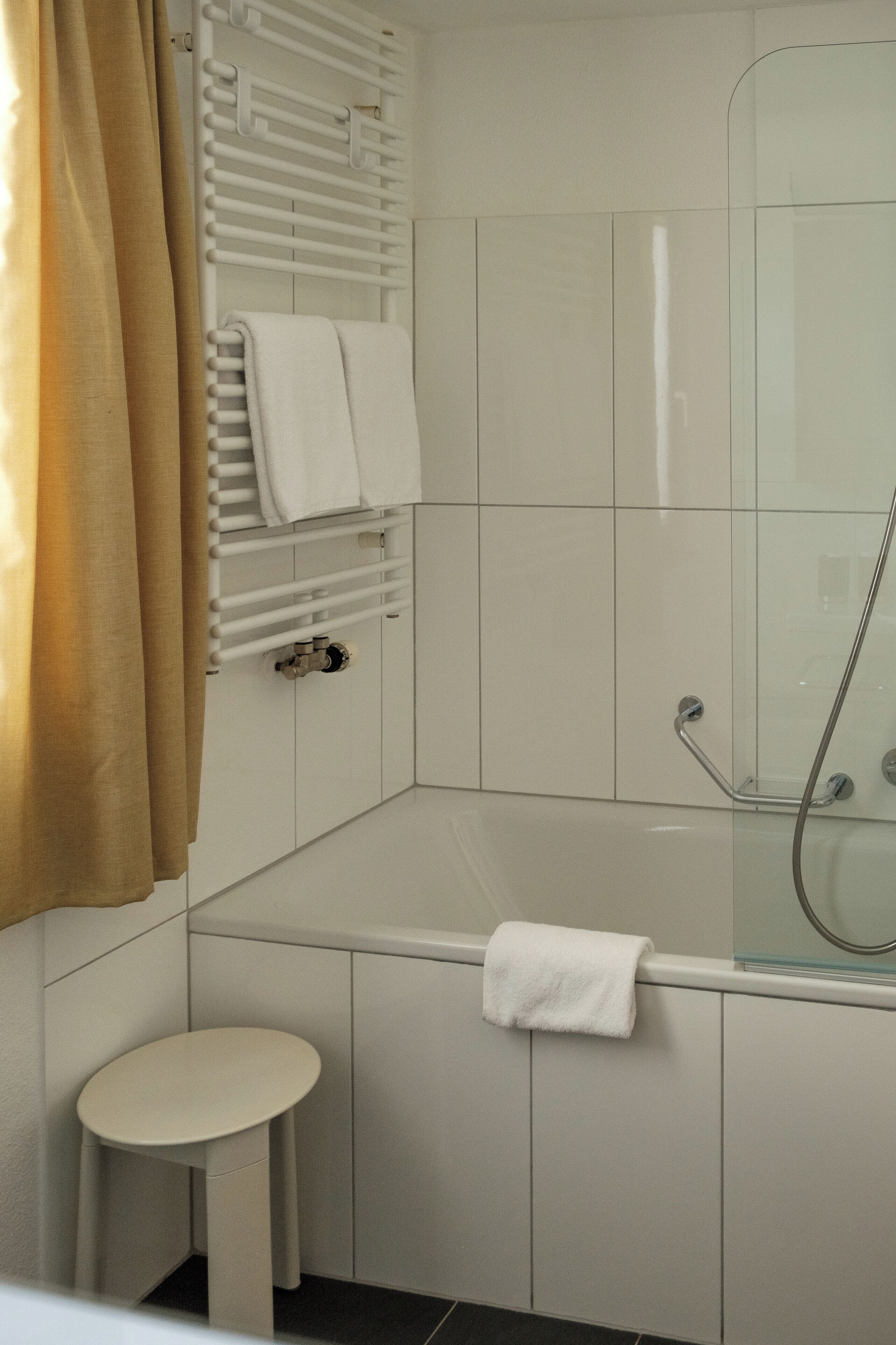 A modern bathroom with a glass-enclosed shower, a white toilet, and a towel rack with multiple towels.
