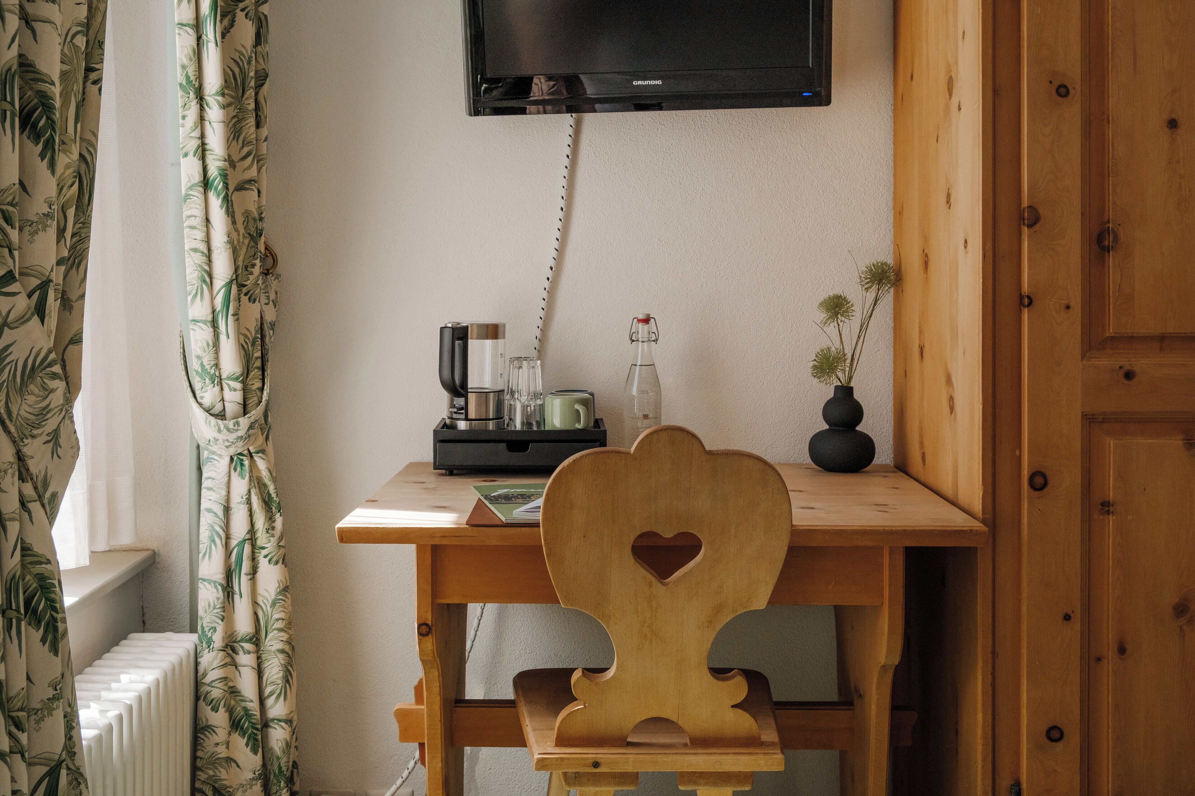 Ein Holztisch mit einem herzförmigen Rücken, ein darüber montierter Fernseher und ein kleiner Blumentopf an der Seite.