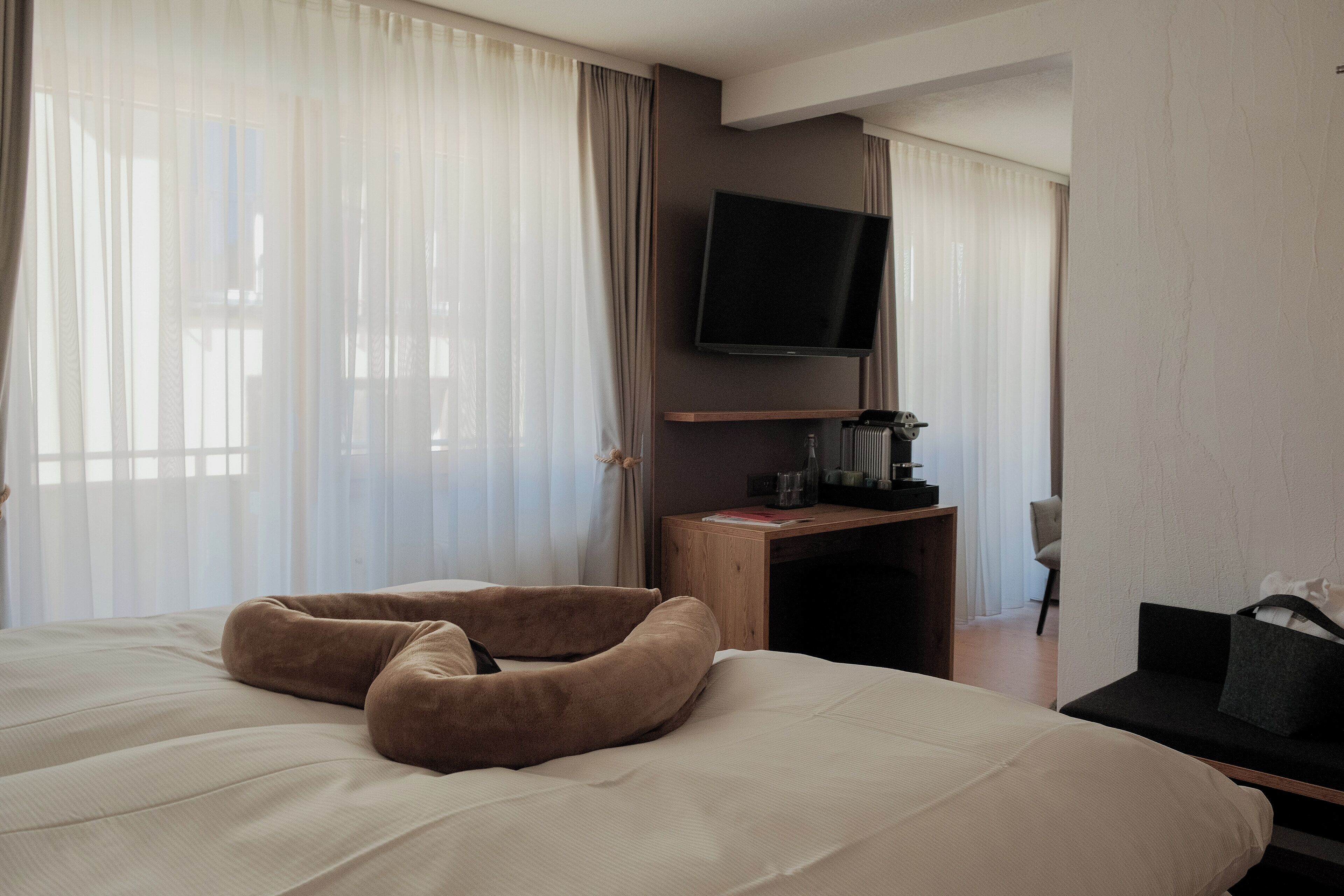 A hotel room with a large bed, a TV mounted on the wall, a wooden desk, and a chair.