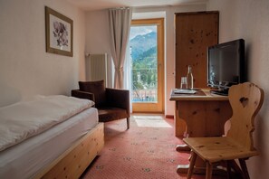 A hotel room with a bed, a desk with a television, a chair, and a view of mountains through the window.
