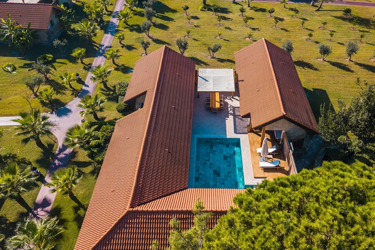 An aerial view of a resort with a swimming pool, a covered patio, and a well-maintained lawn with trees.