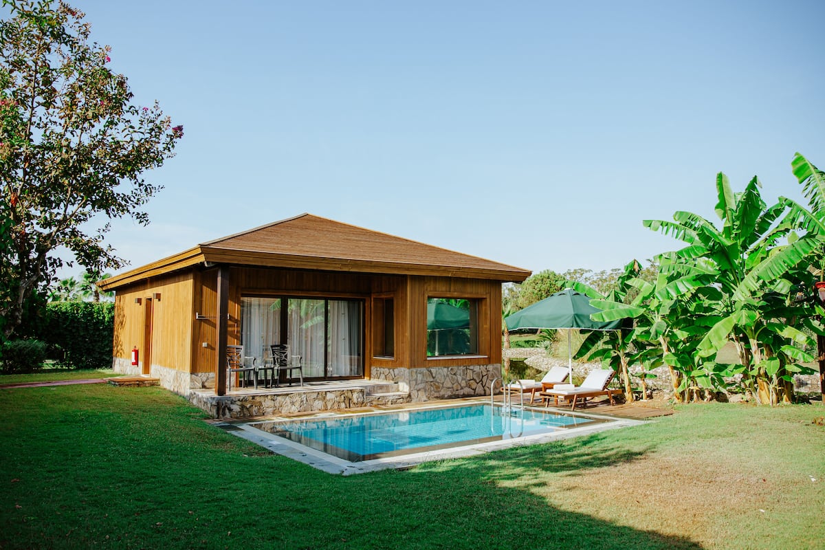 A modern house with a swimming pool, wooden exterior, stone accents, and a patio with lounge chairs.