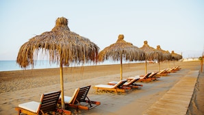 A beach with wooden lounge chairs and thatched umbrellas aligned along the shore. - IC Hotels Green Palace & Villas - All inclusive (Antalya)