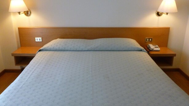 Habitación de hotel estándar con una cama individual, dos mesitas de noche y un teléfono sobre una de ellas.