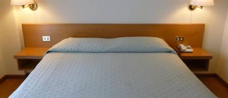Habitación de hotel estándar con una cama individual, dos mesitas de noche y un teléfono sobre una de ellas.