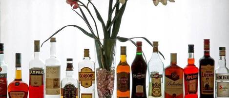 A variety of liquor bottles arranged on a table with a vase of flowers in the center.