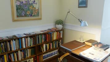 Una biblioteca con scaffali, una scrivania con lampada, un quadro incorniciato e una piccola pianta in vaso.