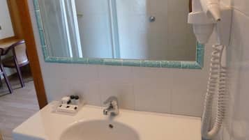A bathroom with a white sink, a mirror with a green frame, and a hairdryer mounted on the wall.