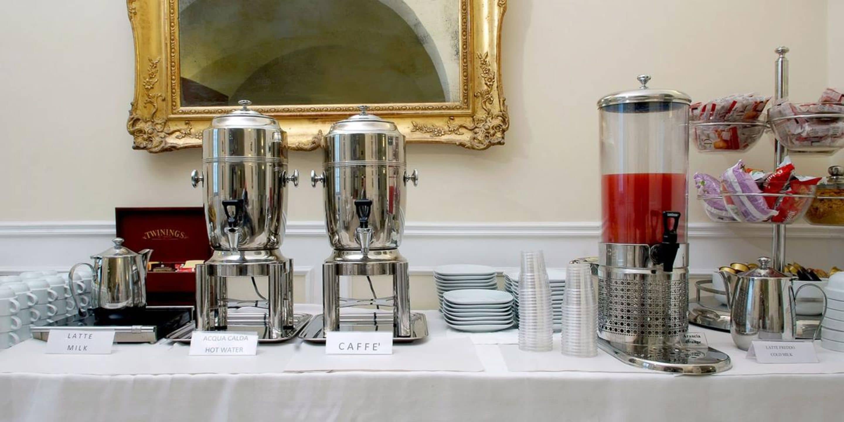 A coffee station with espresso machines, milk, and hot water dispensers, along with a coffee grinder and various coffee pods.