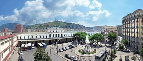 Une place de ville avec un monument central, entourée de bâtiments historiques et sous un ciel dégagé.