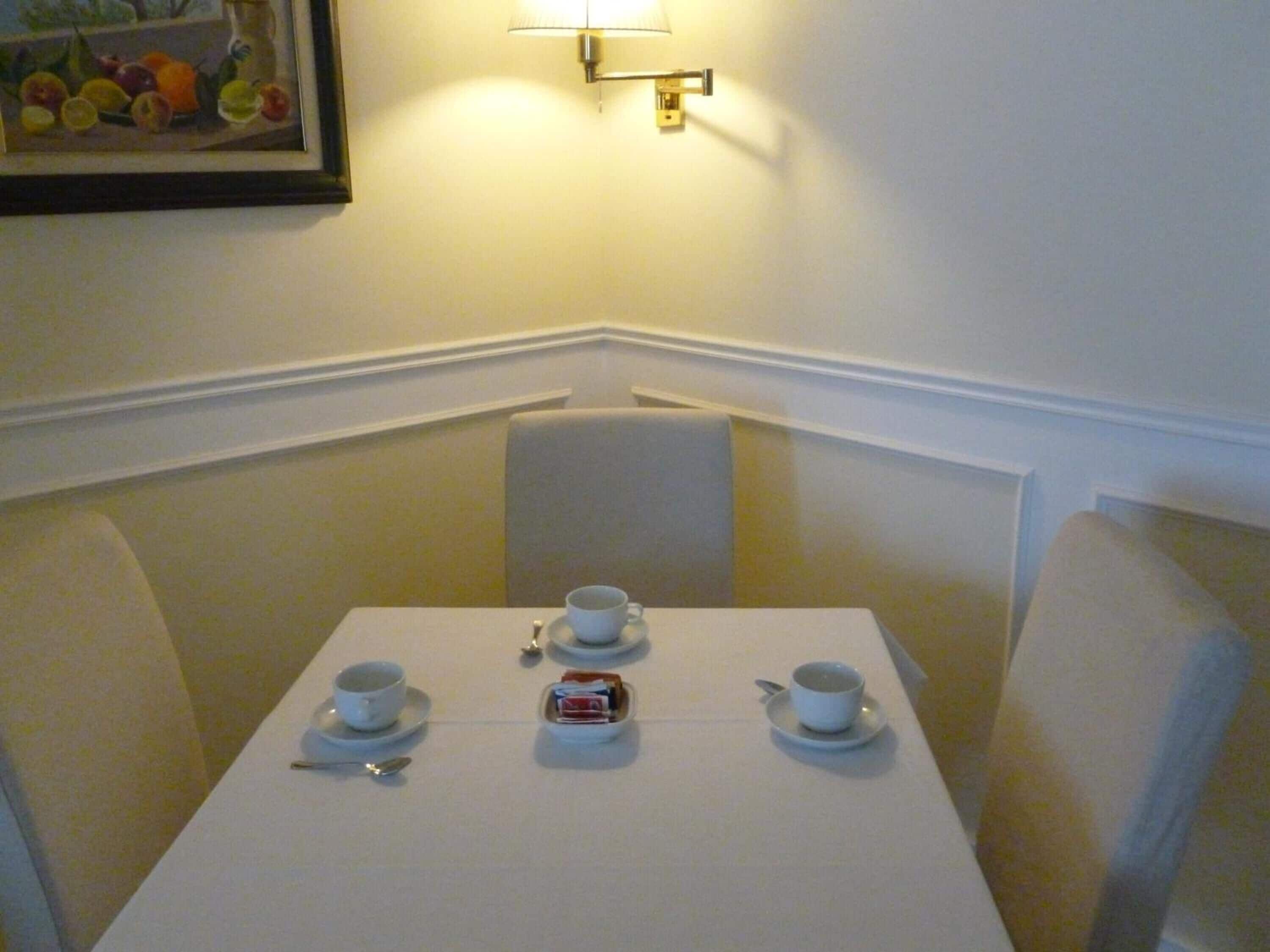 Una mesa de comedor con tres tazas y platillos blancos, una pequeña caja y una cuchara.