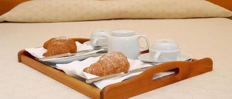 A tray with croissants, a teapot, and cups on a bed.
