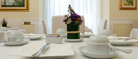 Une table à manger dressée avec de l’assiette blanche, des bols et une théière, et un vase rempli de fleurs placé au centre.
