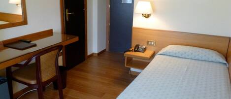 A hotel room with a bed, a desk, a chair, a nightstand with a lamp, and a telephone.