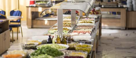 A buffet with various food options, including salads, fruits, and desserts, arranged on a long table.