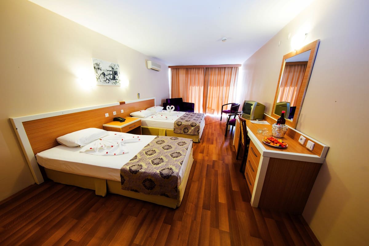 Ein Hotelzimmer mit zwei Betten, einem Schreibtisch, einem Stuhl, einem Spiegel und einer kleinen Küchenzeile.