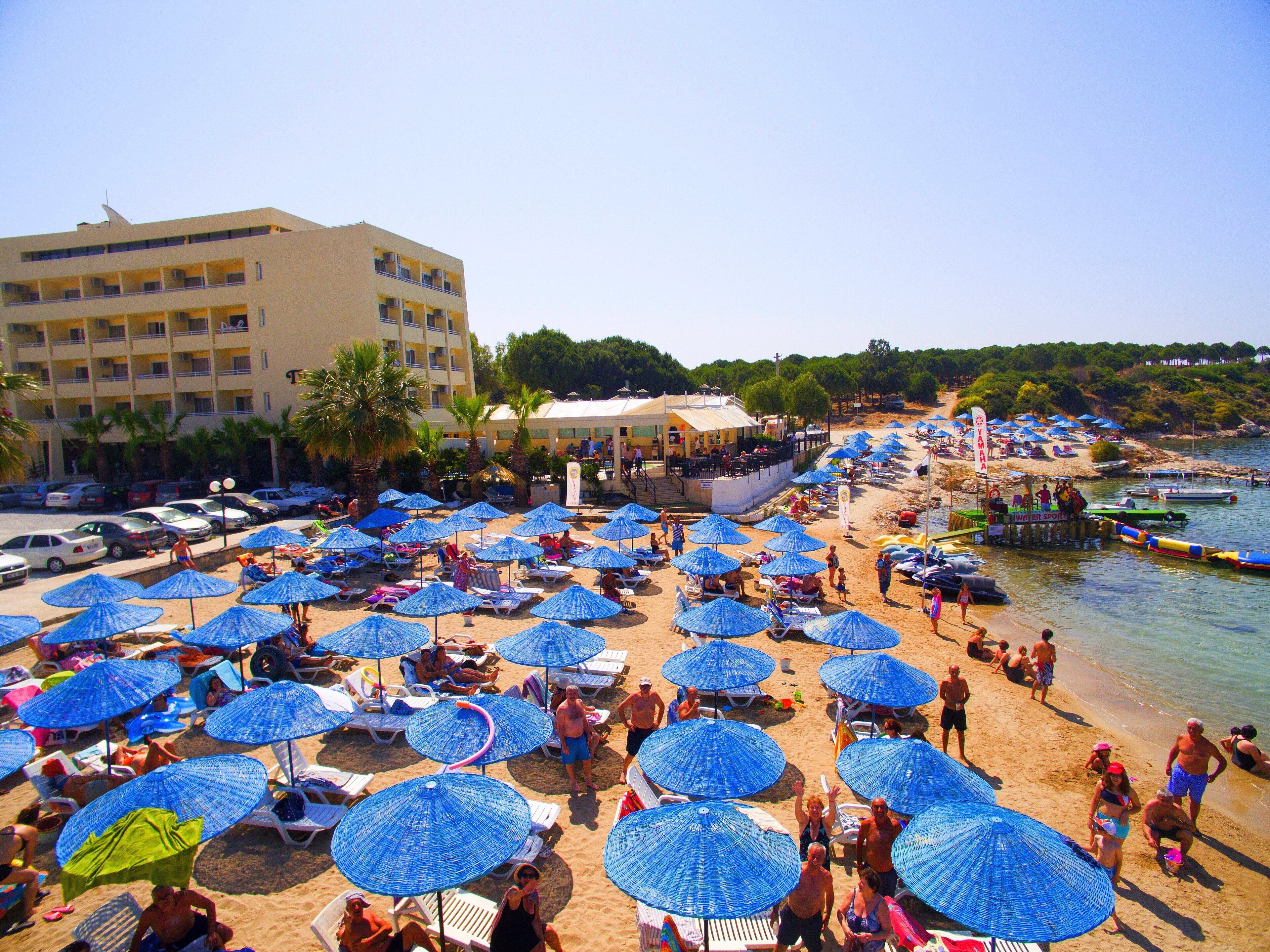 Une plage parsemée de nombreux parasols bleus, un immeuble doté de balcons et une zone dédiée aux sports nautiques.
