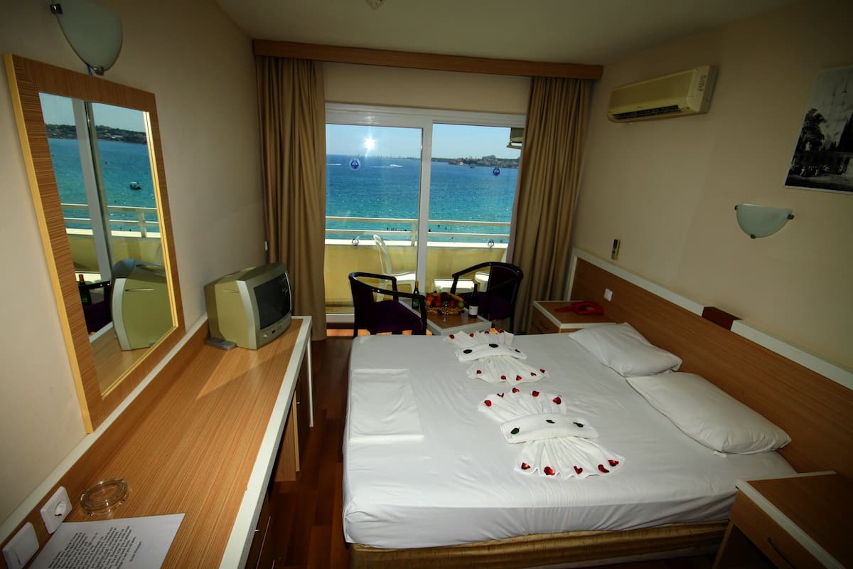 Ein Hotelzimmer mit Bett, Fernseher, Schreibtisch, Stuhl und Meerblick.