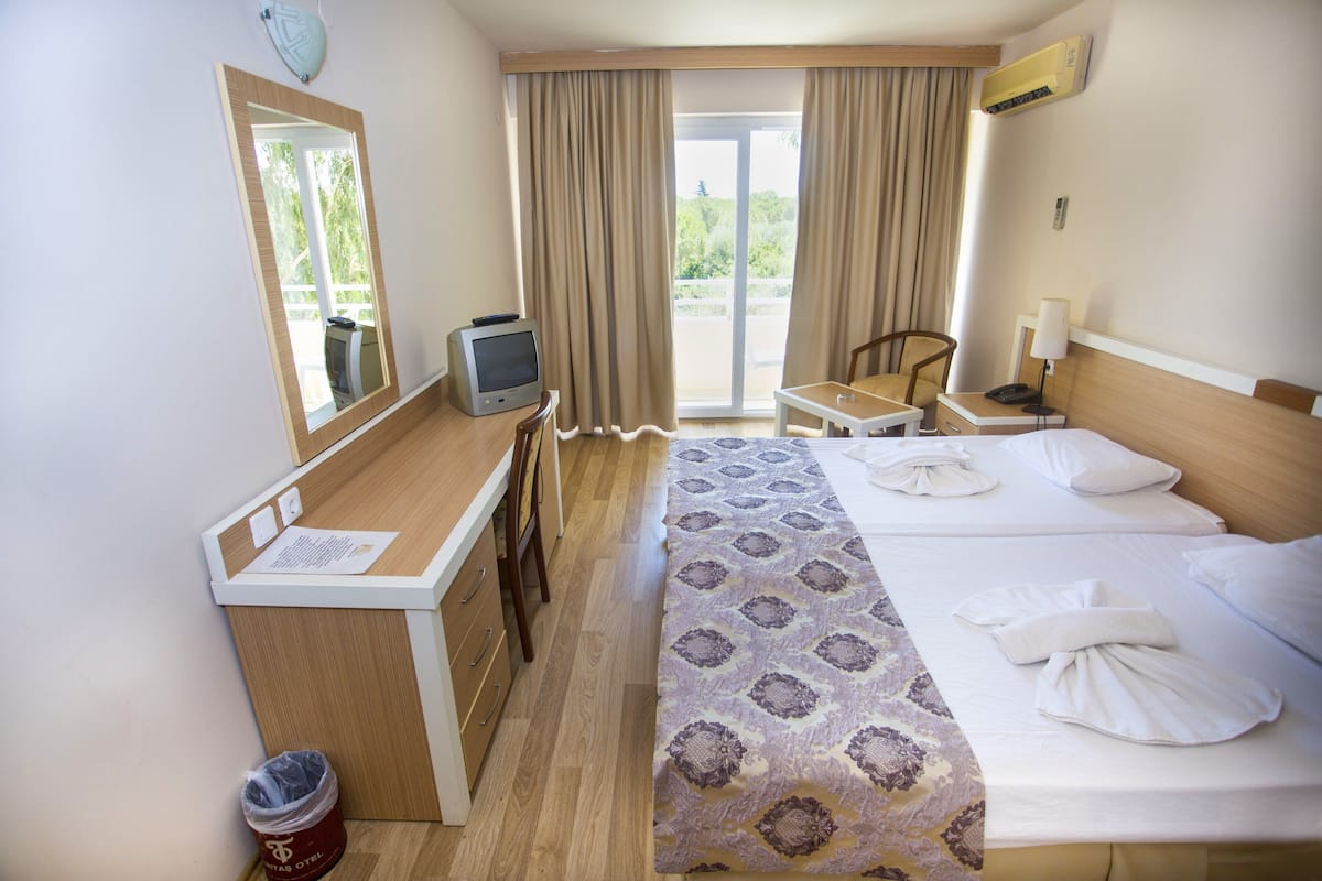 Ein Hotelzimmer mit Bett, Schreibtisch, Stuhl, Fernseher und einem Fenster mit Vorhängen.