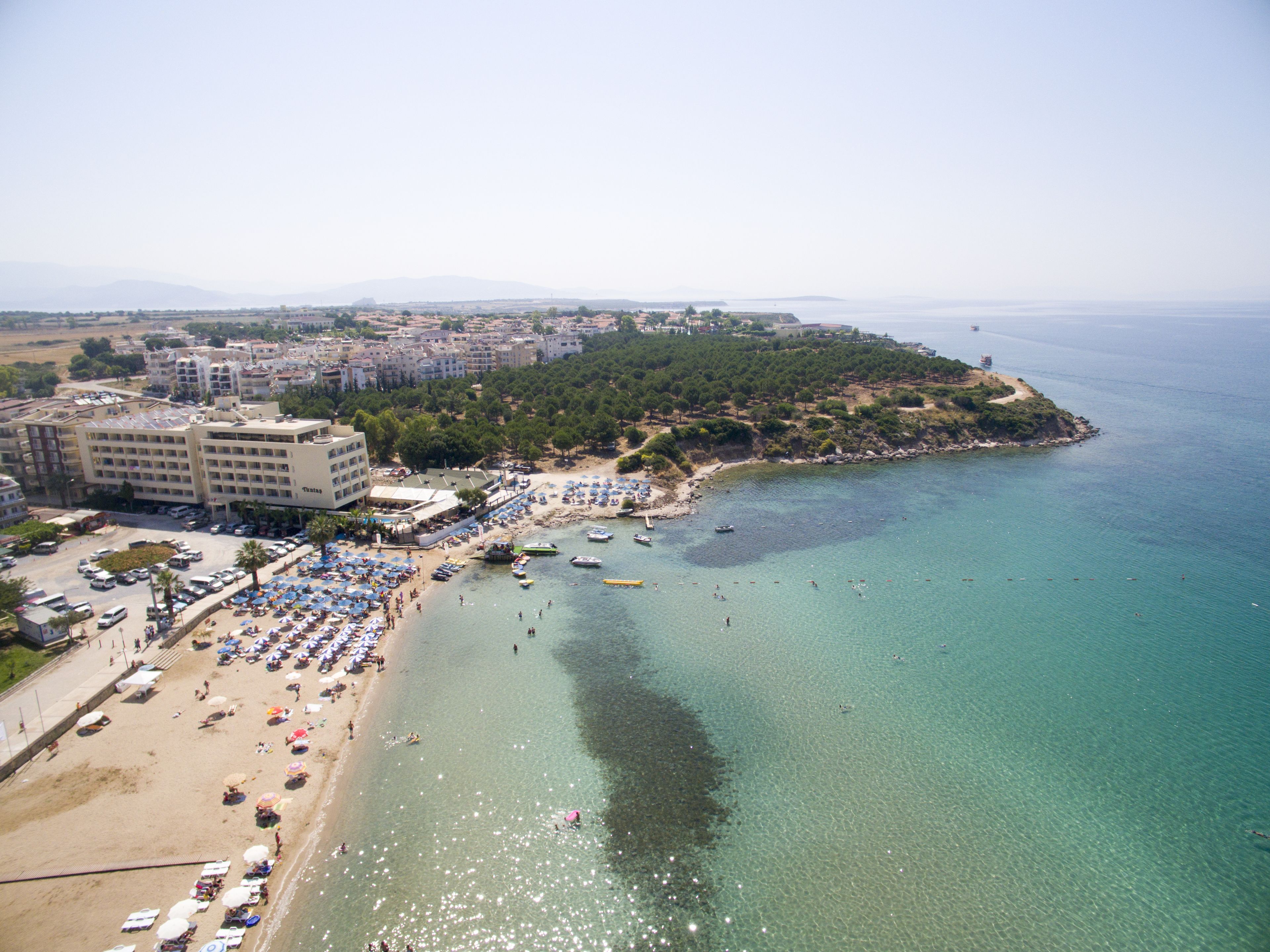 A coastal hotel with a beach, clear waters, and a mountainous backdrop.