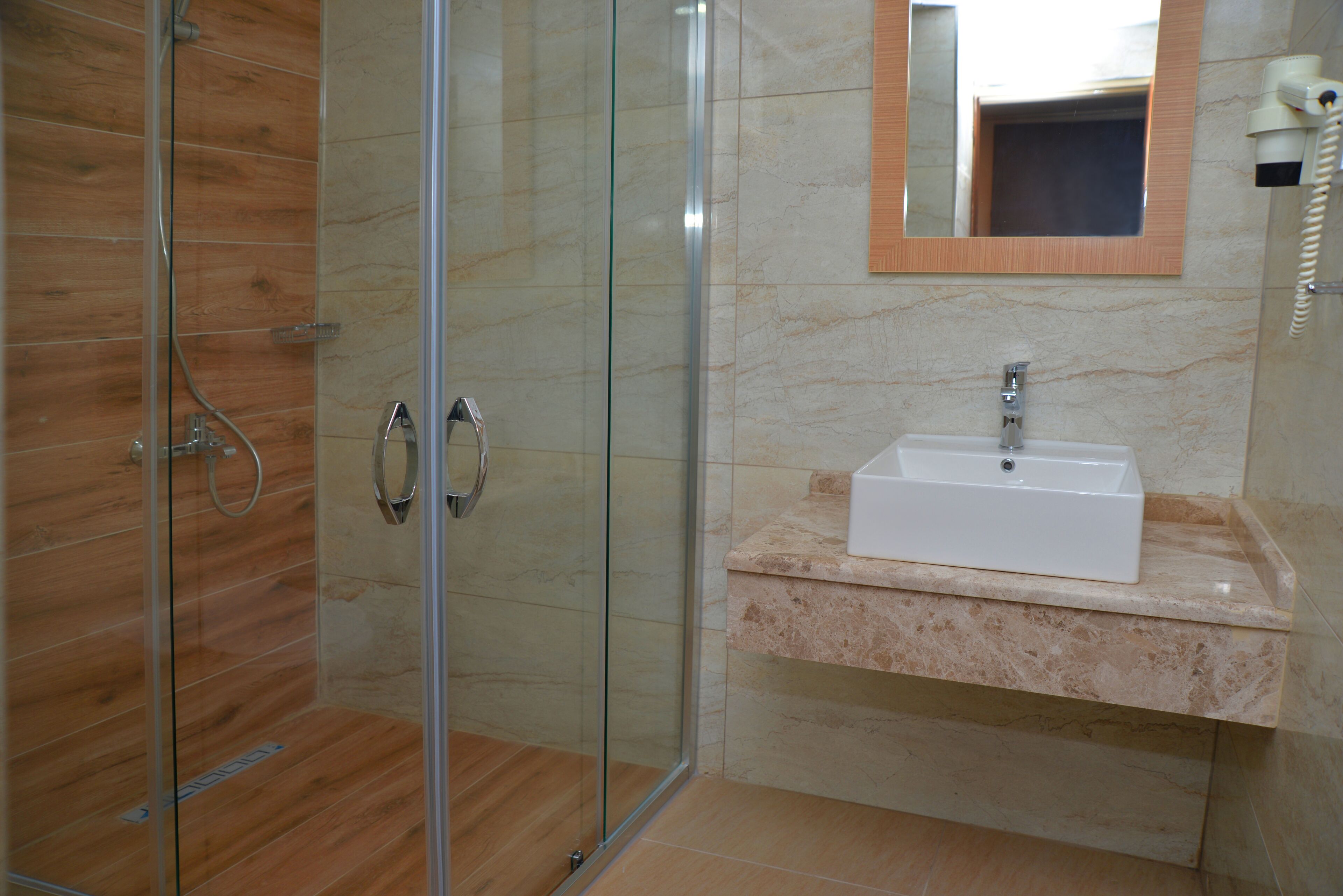 A modern bathroom with a glass-enclosed shower, a marble-tiled floor, and a white sink with a mirror above it.