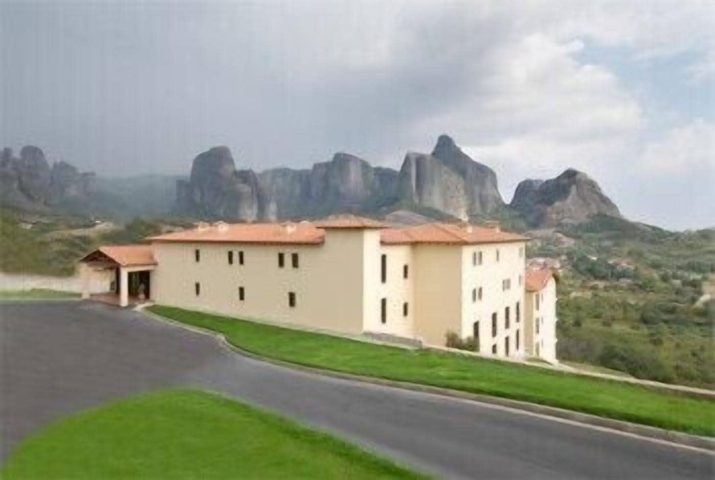 A building with a flat roof and multiple windows, surrounded by a green landscape and mountains in the background.