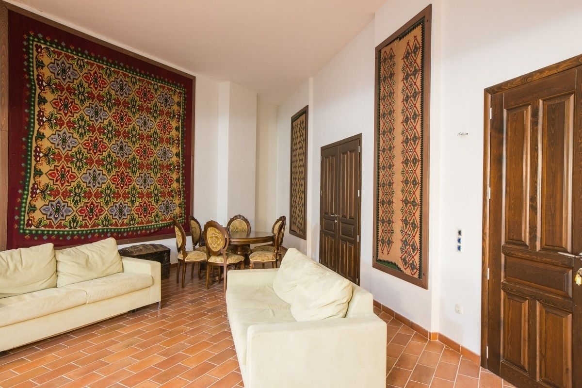 A living room with a sofa, a dining table with chairs, and a large decorative tapestry on the wall.