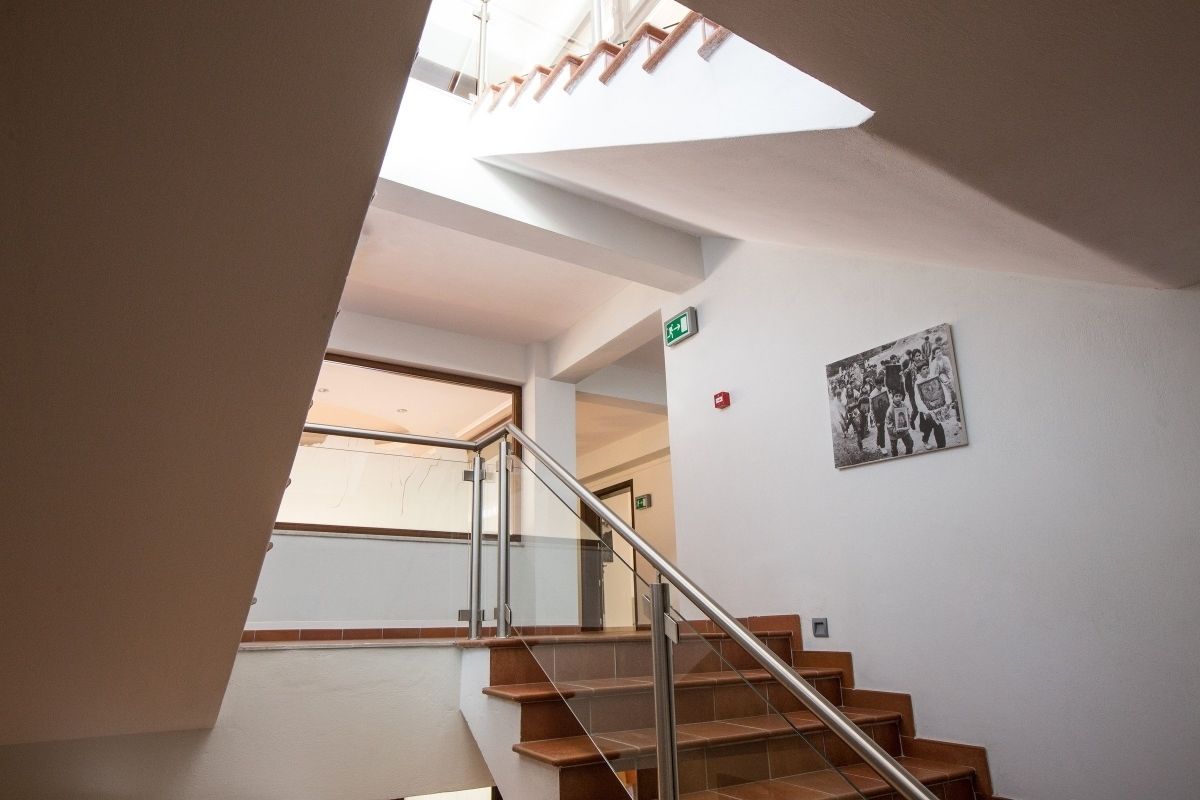 A staircase with glass railings and wooden steps, leading to a room with a white wall and a black-and-white photo.
