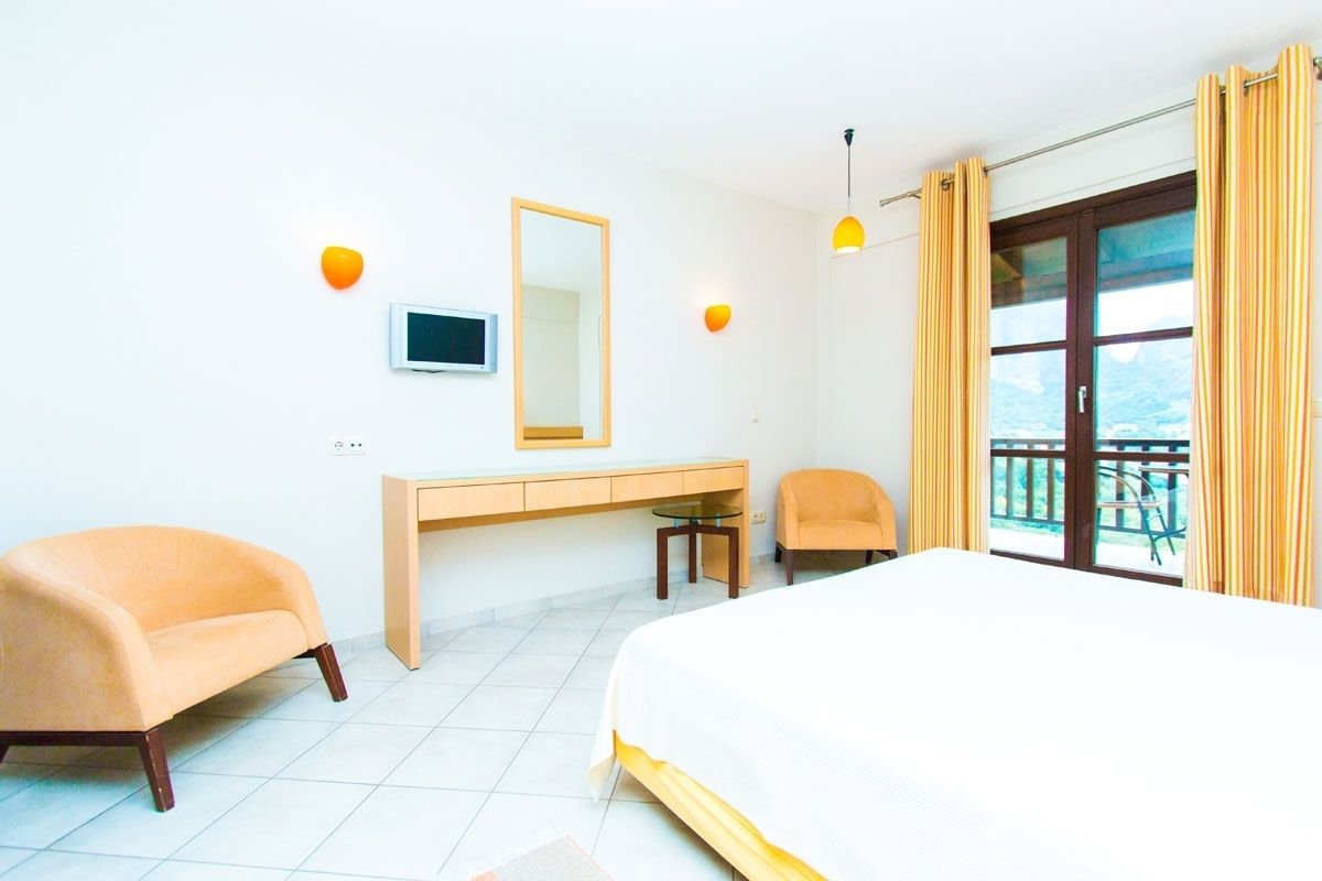 A hotel room with a bed, a desk, a chair, a mirror, and a view of the outdoors.