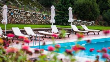 A pool area with lounge chairs and umbrellas, surrounded by a stone wall and greenery.