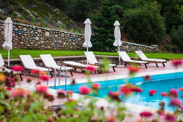 Un espace piscine agrémenté de chaises longues et de parasols, entouré d’un mur de pierre et de verdure.