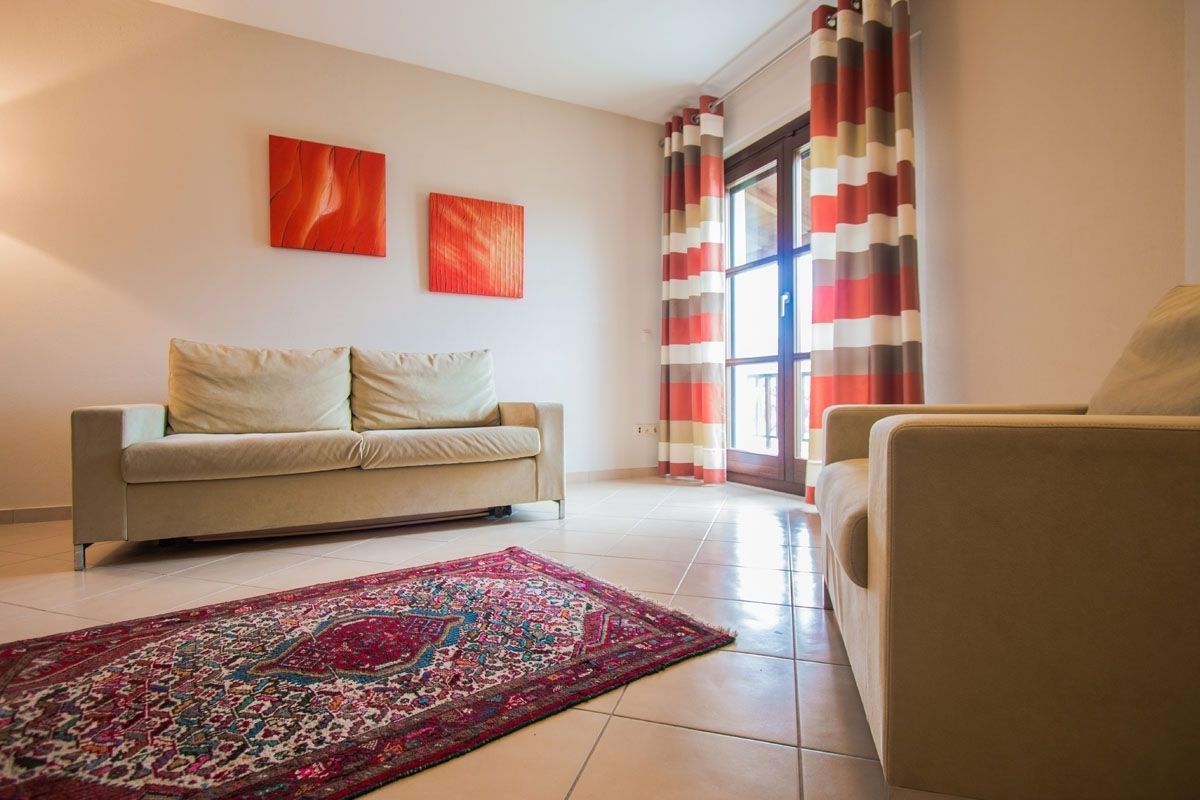 A living room with a beige sofa, a patterned rug, and two abstract paintings on the wall.