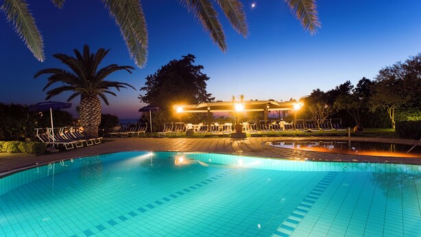 Une piscine avec des chaises longues et des palmiers, au crépuscule.