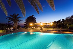 Una piscina con sillones de descanso y palmeras al atardecer.