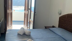 A bedroom with a bed, two rolled towels, and an open door leading to a balcony with a view of the sea. - Oltremare (Lipari)