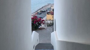 A staircase leading to a balcony with a view of a coastal area, including a beach and parked cars. - Oltremare (Lipari)